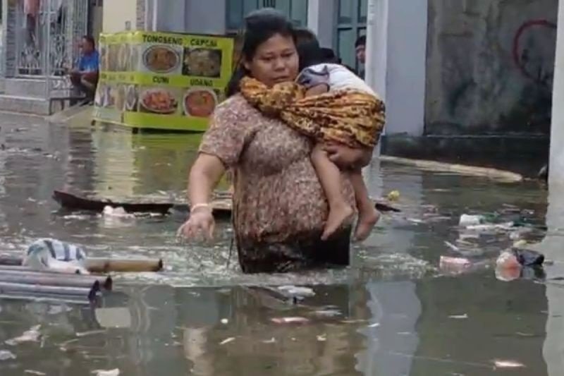 Seorang wanita menggendong bayi melintasi genangan banjir rob di kawasan Muara Angke Penjaringan Jakarta Utara pada Senin (16/12/2024). Foto: ANTARA